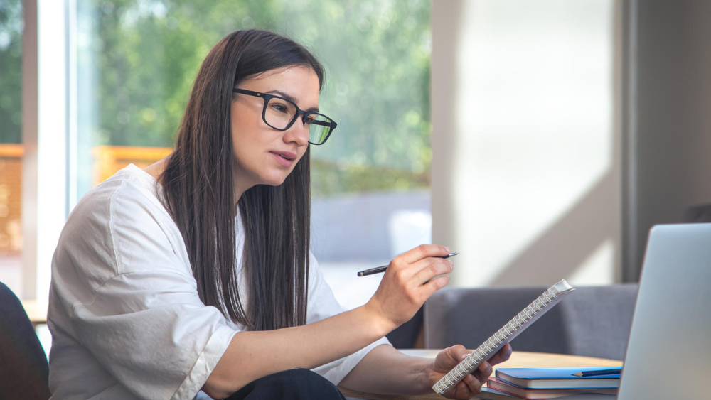 Agente de seguros estudiando y tomando notas en laptop para mejorar sus habilidades de venta y mantenerse actualizada